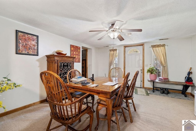 dining room with a textured ceiling, baseboards, a ceiling fan, and light colored carpet