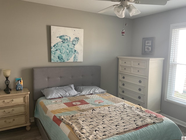 bedroom featuring ceiling fan, multiple windows, baseboards, and wood finished floors