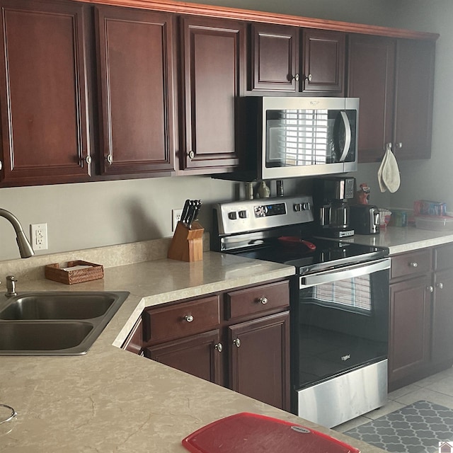 kitchen featuring dark brown cabinetry, tile patterned flooring, stainless steel appliances, light countertops, and a sink