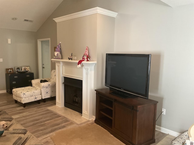 living room featuring light wood finished floors, lofted ceiling, visible vents, a fireplace with flush hearth, and baseboards