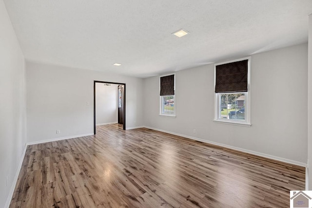 spare room featuring a textured ceiling, baseboards, and wood finished floors