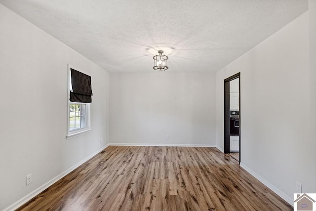 spare room with a notable chandelier, a textured ceiling, baseboards, and wood finished floors