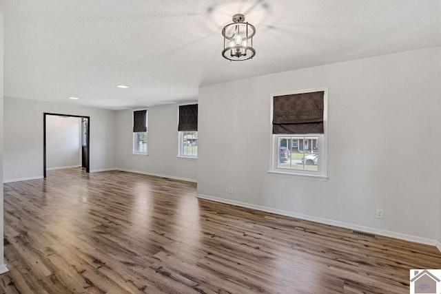 spare room with visible vents, baseboards, a chandelier, and wood finished floors