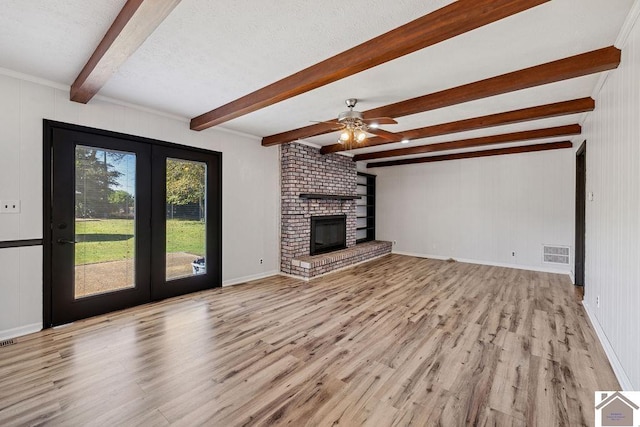 unfurnished living room featuring a brick fireplace, visible vents, wood finished floors, and beamed ceiling