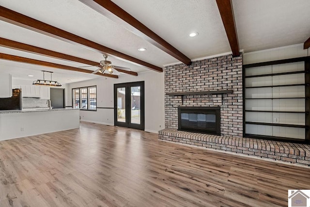 unfurnished living room with a fireplace, ceiling fan, wood finished floors, beamed ceiling, and baseboards