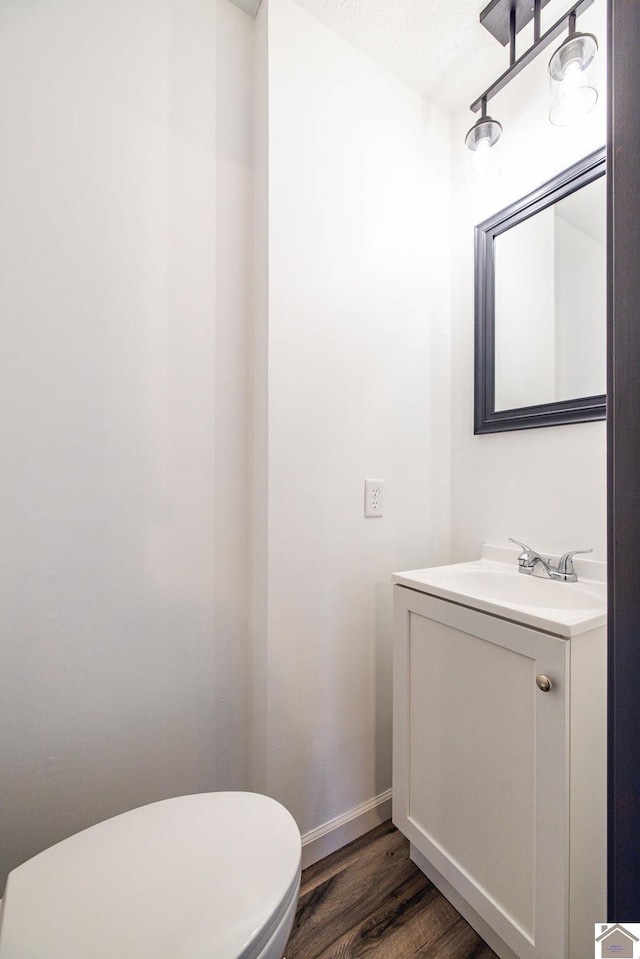 half bath featuring toilet, baseboards, wood finished floors, and vanity