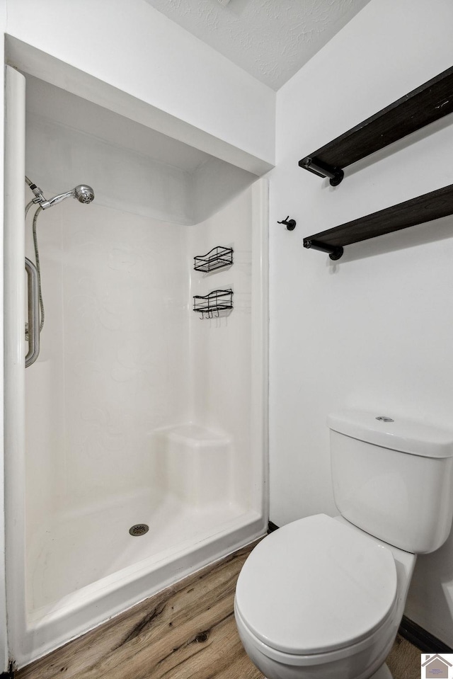 bathroom with a stall shower, a textured ceiling, toilet, and wood finished floors