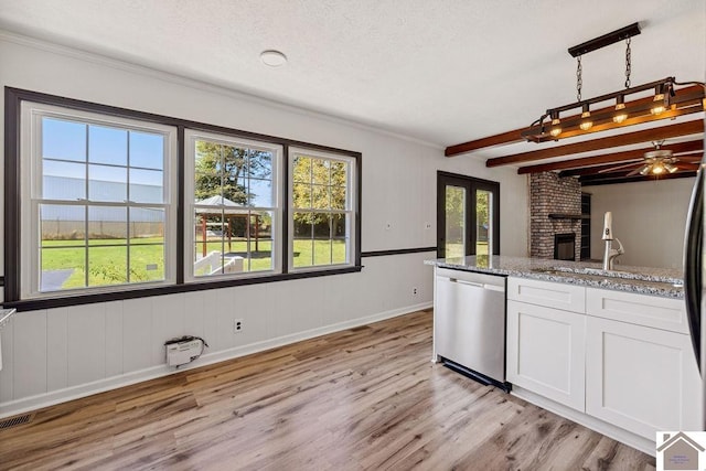 kitchen with beam ceiling, a fireplace, stainless steel dishwasher, white cabinetry, and light wood-type flooring