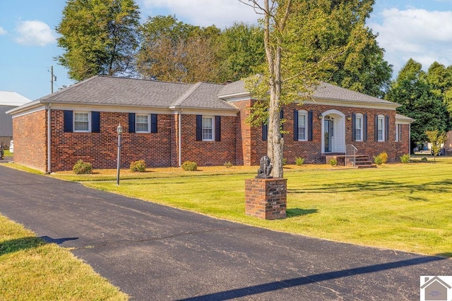 view of front of home featuring a shingled roof, a front yard, and brick siding