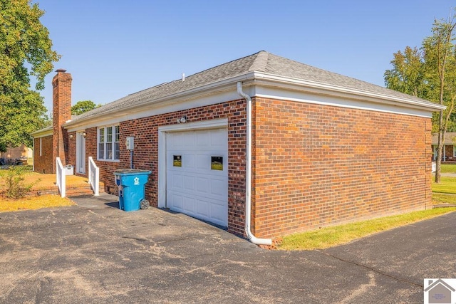 view of home's exterior featuring aphalt driveway, a garage, brick siding, a shingled roof, and a chimney