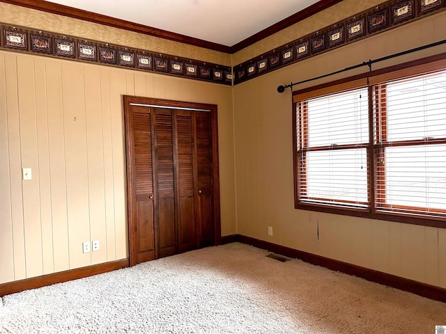 unfurnished bedroom featuring baseboards, visible vents, crown molding, carpet floors, and a closet