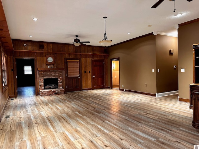 unfurnished living room with wood walls, a fireplace, baseboards, light wood finished floors, and crown molding