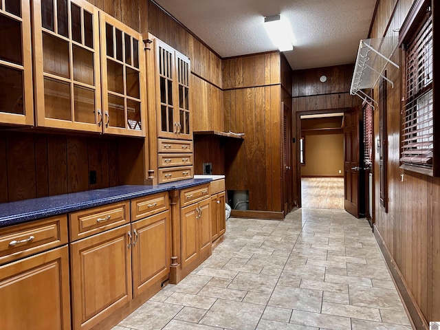 kitchen with a textured ceiling, wood walls, glass insert cabinets, and brown cabinetry