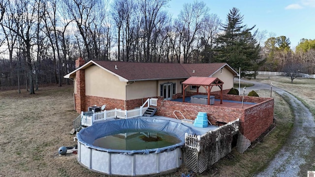 back of property featuring a chimney, stucco siding, a gazebo, a patio area, and a covered pool