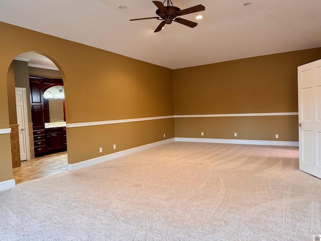 spare room with arched walkways, light colored carpet, vaulted ceiling, ceiling fan, and baseboards