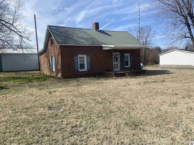 rear view of house featuring metal roof, brick siding, a lawn, and a chimney