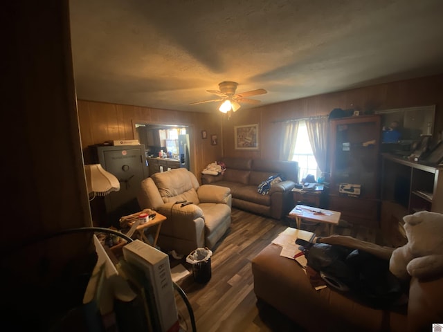 living area with a ceiling fan, wooden walls, a textured ceiling, and wood finished floors