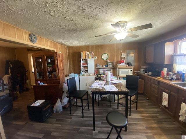 dining space with a ceiling fan, wooden walls, a textured ceiling, and wood finished floors