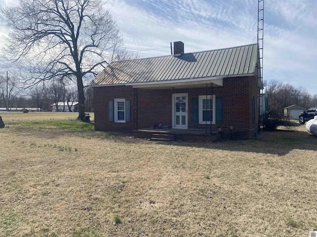 rear view of property featuring a porch, metal roof, brick siding, and a lawn