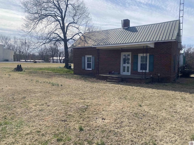 rear view of property featuring covered porch, brick siding, metal roof, and a lawn