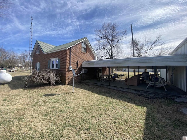 view of property exterior featuring metal roof, brick siding, a lawn, and a patio area