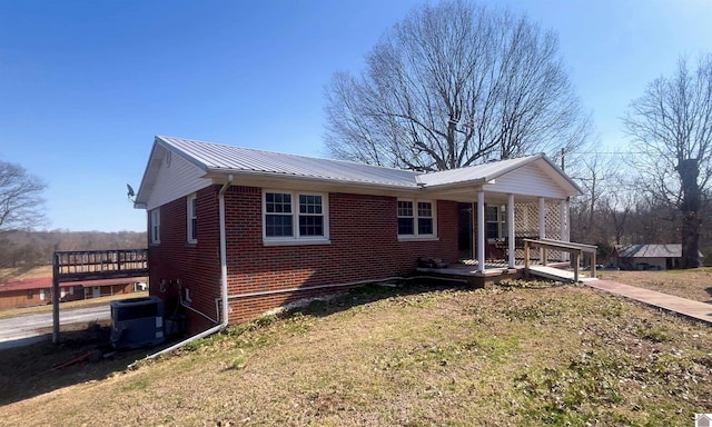 view of front facade with metal roof, a porch, central air condition unit, brick siding, and a front lawn