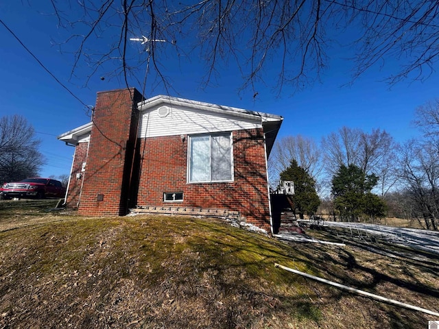 view of property exterior with a yard, a chimney, and brick siding