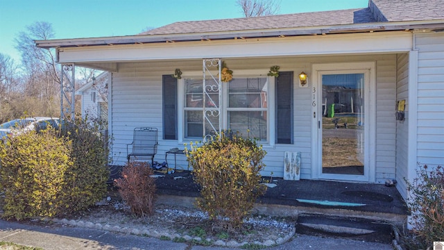 view of exterior entry featuring a porch and roof with shingles