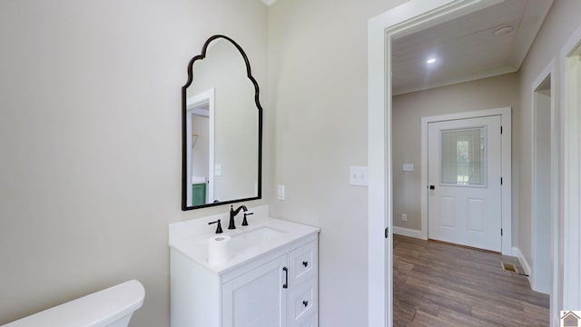 half bath with visible vents, baseboards, toilet, wood finished floors, and vanity