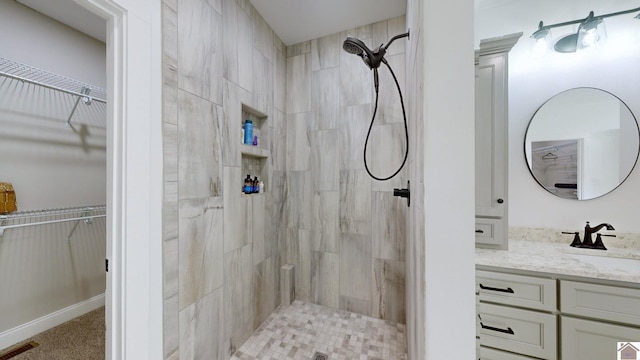 full bath with vanity, a spacious closet, a tile shower, and visible vents