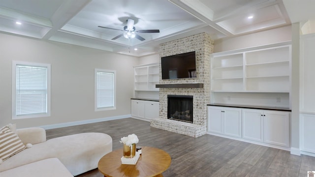 living area with ceiling fan, a fireplace, coffered ceiling, baseboards, and dark wood finished floors