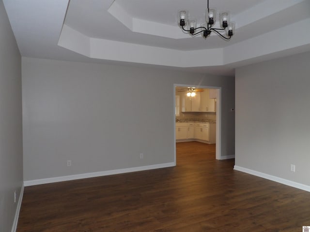 empty room featuring dark wood-style floors, ceiling fan with notable chandelier, a raised ceiling, and baseboards