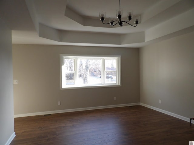 empty room with baseboards, a tray ceiling, dark wood finished floors, and an inviting chandelier