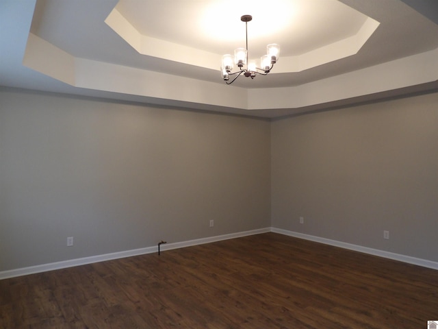 spare room featuring dark wood-type flooring, a tray ceiling, and a chandelier