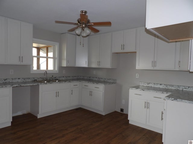 kitchen with light stone counters, dark wood-type flooring, a sink, and white cabinetry