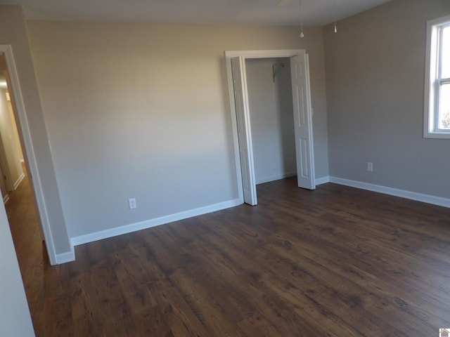 unfurnished bedroom featuring a closet, dark wood finished floors, and baseboards