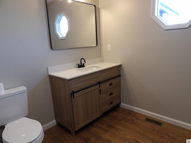 half bathroom with baseboards, visible vents, toilet, and wood finished floors