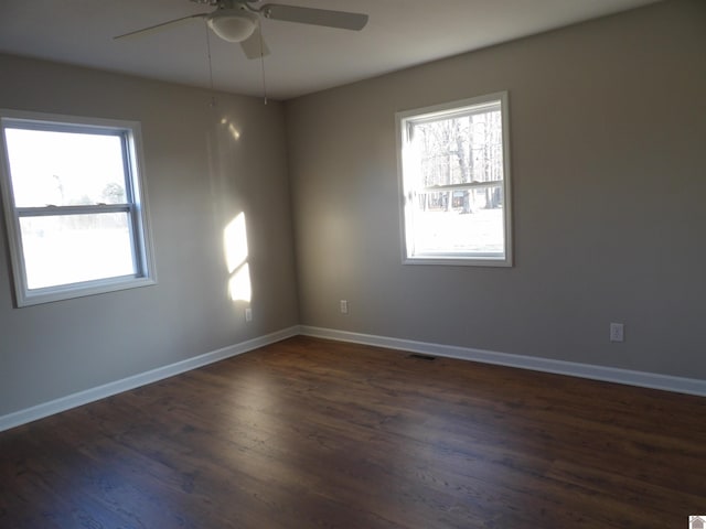 empty room featuring dark wood-style floors, plenty of natural light, visible vents, and baseboards