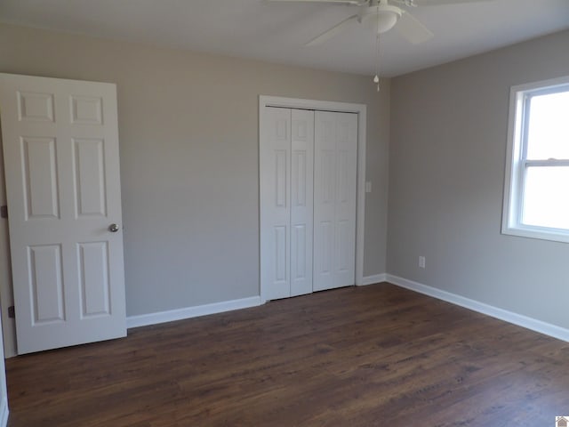 unfurnished bedroom with a closet, dark wood finished floors, baseboards, and ceiling fan