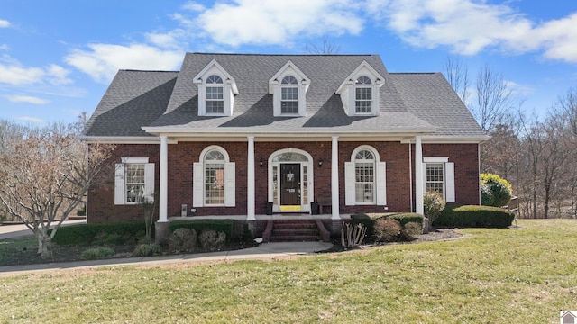 view of front of property with covered porch, roof with shingles, a front lawn, and brick siding