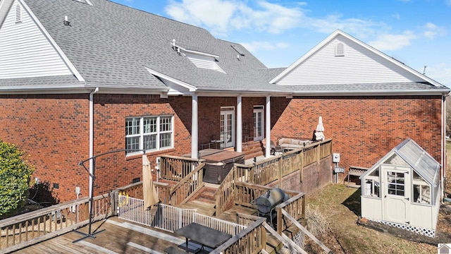 rear view of house featuring a shingled roof, brick siding, an outdoor structure, and a deck