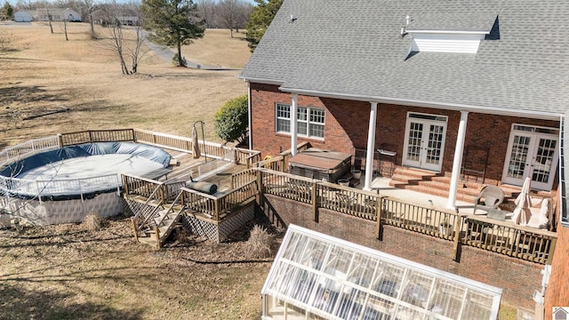 exterior space with french doors, a shingled roof, a wooden deck, and brick siding