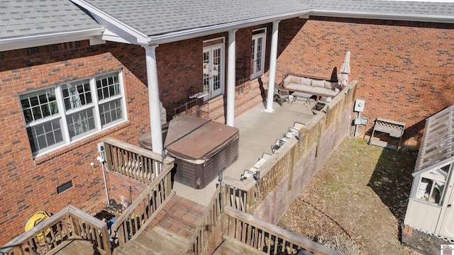 exterior space with a hot tub, a patio, roof with shingles, crawl space, and brick siding