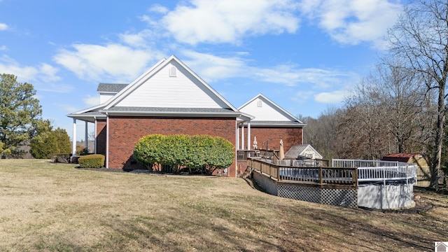 back of property featuring brick siding, a lawn, and a wooden deck