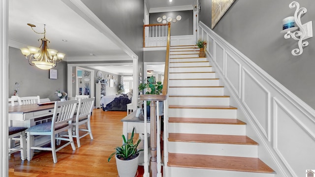 stairway with a decorative wall, ornamental molding, wainscoting, wood finished floors, and a chandelier