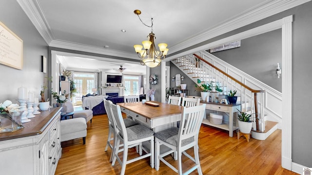 dining area featuring ornamental molding, stairs, light wood-type flooring, a fireplace, and ceiling fan with notable chandelier