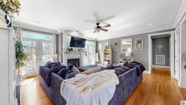 living area with light wood finished floors, visible vents, crown molding, french doors, and a fireplace