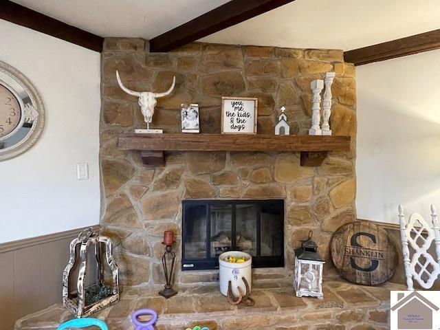 interior details featuring wainscoting, beamed ceiling, and a stone fireplace