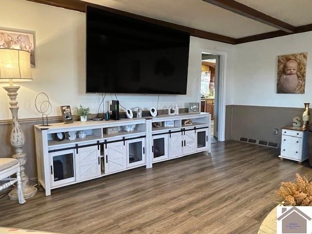 living room featuring a wainscoted wall, visible vents, beam ceiling, and wood finished floors