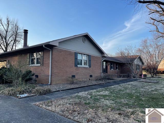 view of property exterior with crawl space, a yard, and brick siding